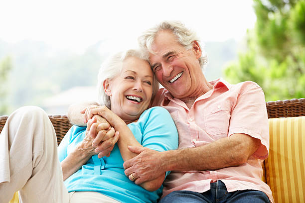 Senior Couple Sitting On Outdoor Seat Together Laughing